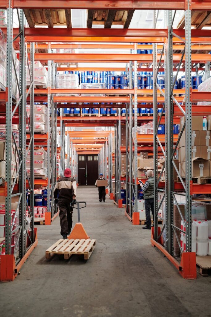 pexels-photo-4483772-4483772 Workers arrange inventory on shelves in a large industrial warehouse.