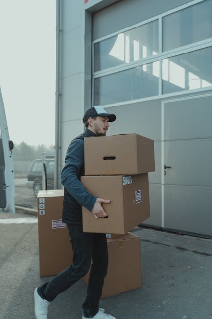 pexels-photo-6169059-6169059 A delivery man carrying cardboard boxes to a loading dock outside an industrial building.