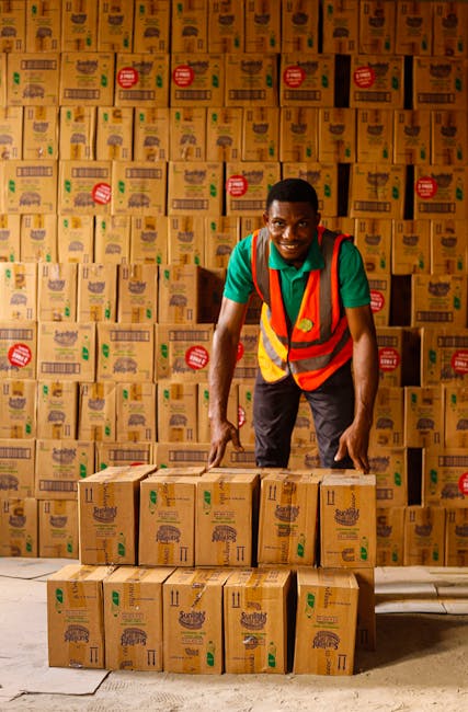 pexels-photo-8069547-8069547 Smiling warehouse worker organizing stacks of boxes with a reflective vest indoors.
